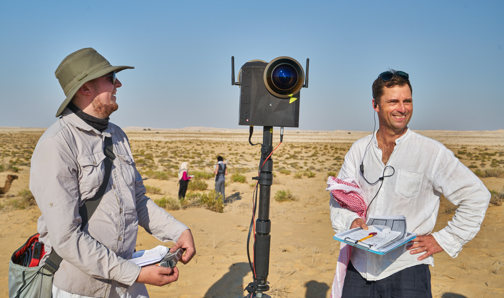 Two crew members with the Meta camera on a tall pole in the Qatari desert.