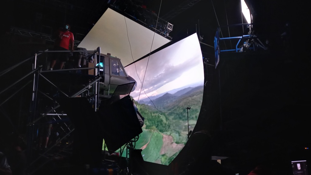 A helicopter set in a virtual production studio, surrounded by a curved LED screen showing aerial footage.