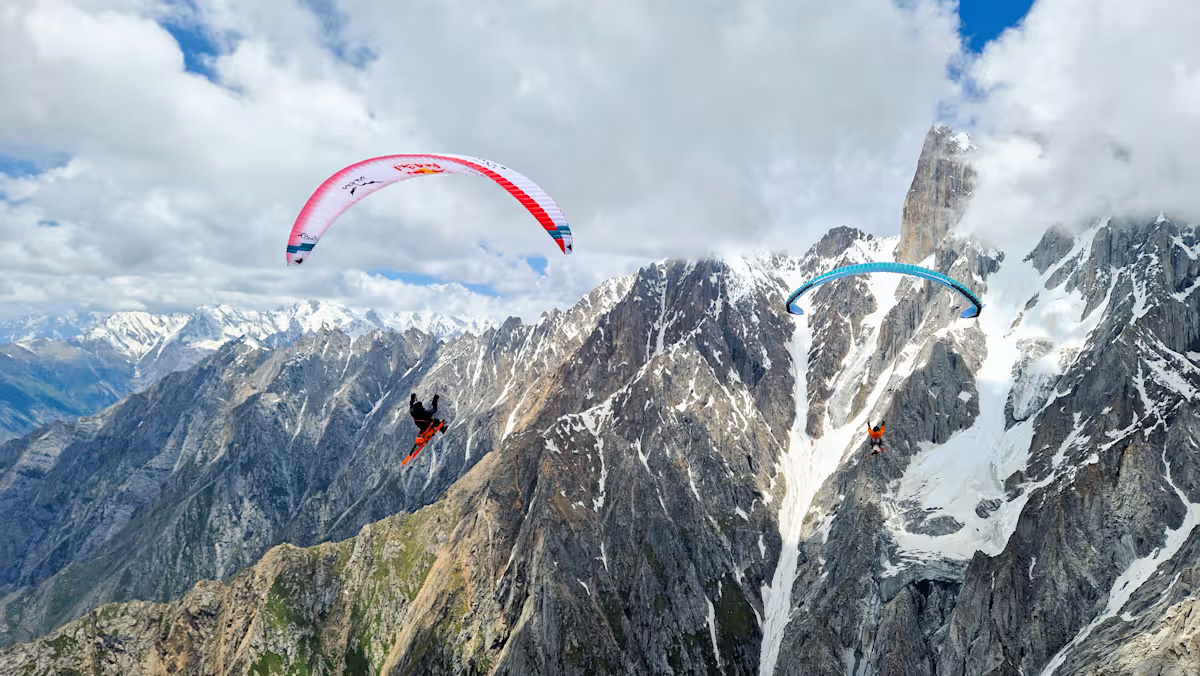 A paraglider flies over a ridge of snow-covered alpine peaks.