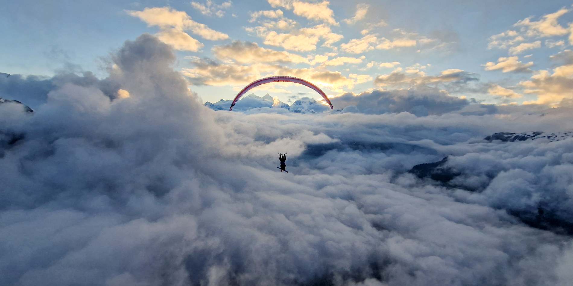 A paraglider above a sea of cloud at sunset.