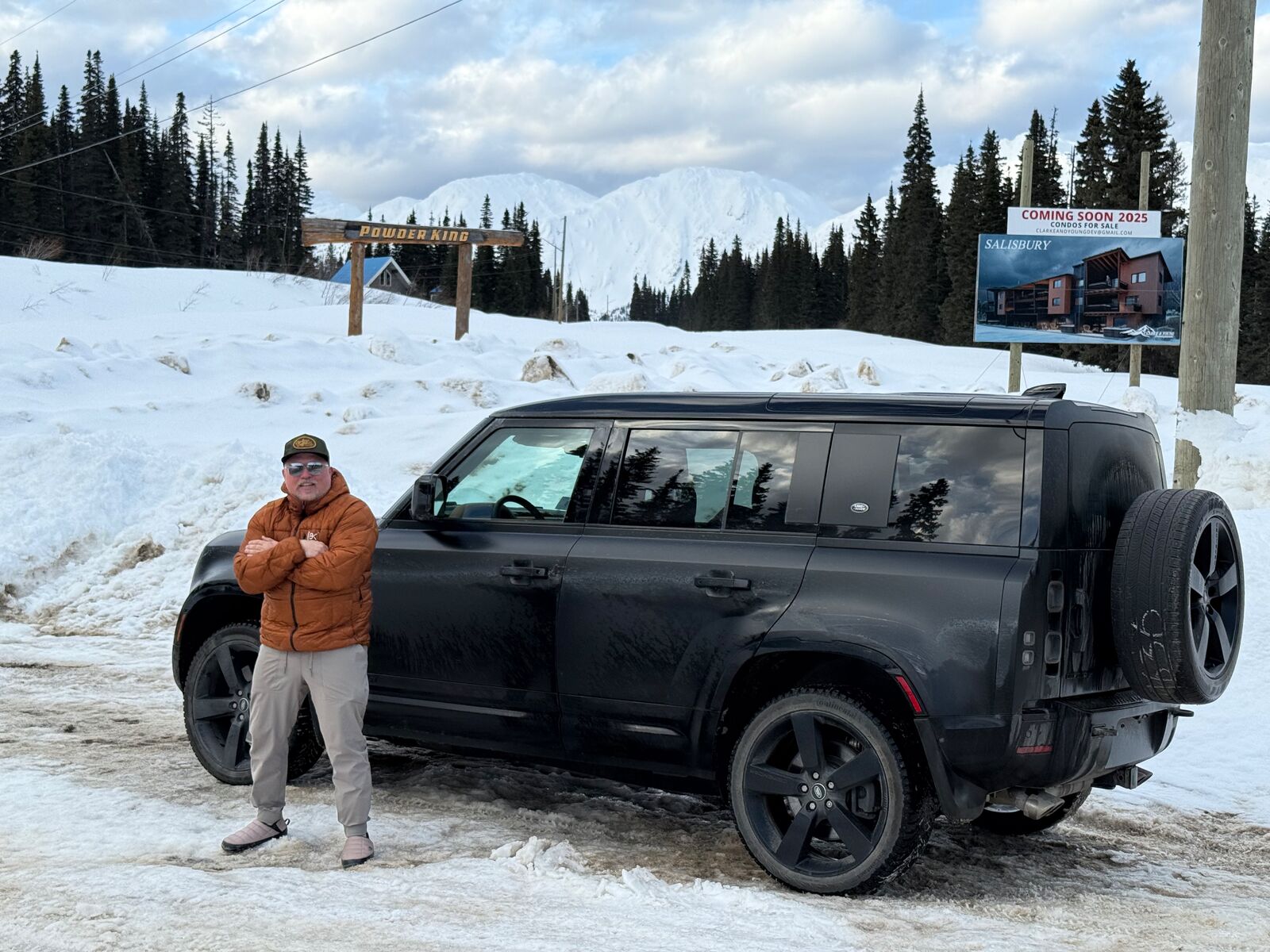 A crew member stands beside a black Land Rover Defender in the snow.