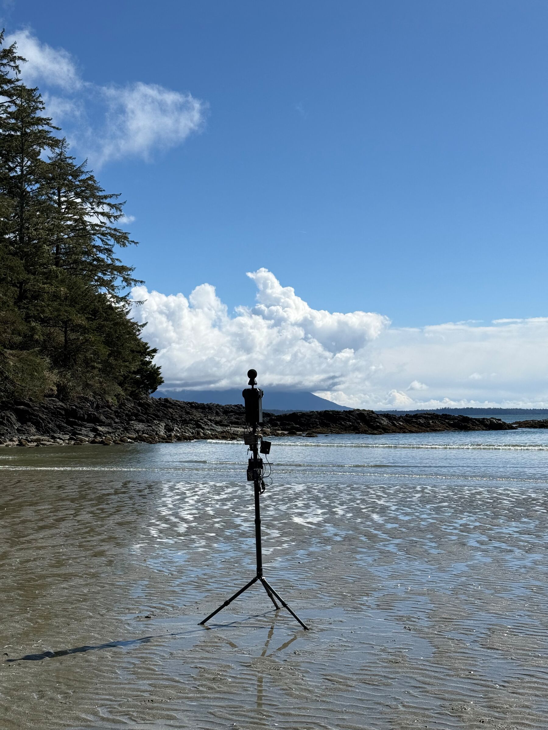 The Meta Four stands alone on a wide, wet tidal beach under a blue sky.