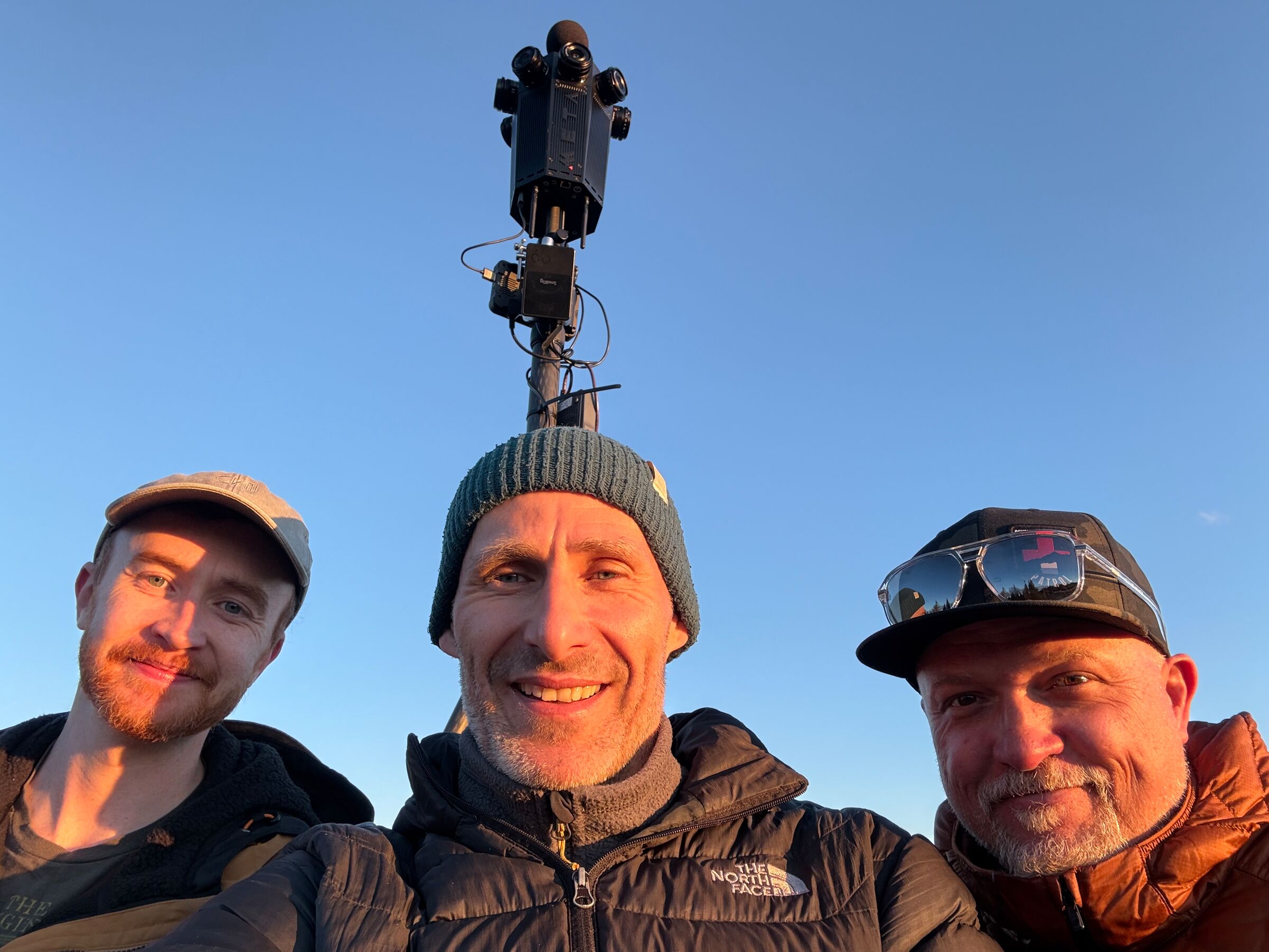 Three crew members take a selfie at sunset beneath the Meta Four on its mast.